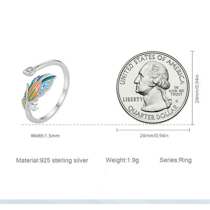 Um anel de prata 925 com uma pena colorida e pedras brilhantes na parte superior, comparação da largura de 1.5mm do anel com a largura de 0.94mm de uma moeda de 0.25 cents.